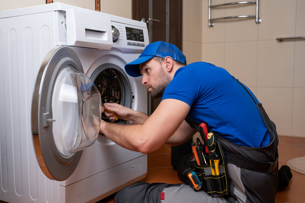Working man plumber repairs a washing machine in home. Washing machine installation or repair. plumber connecting appliance.